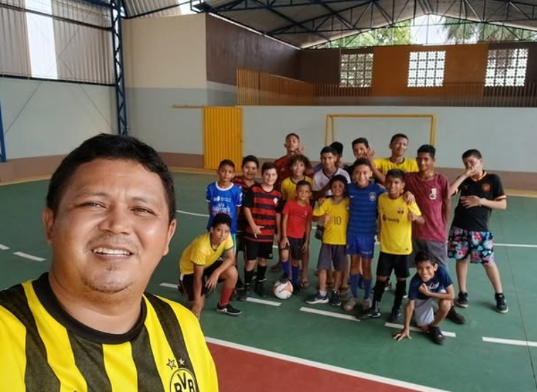 Jogo de futebol de crianças e adolescentes em quadra coberta.